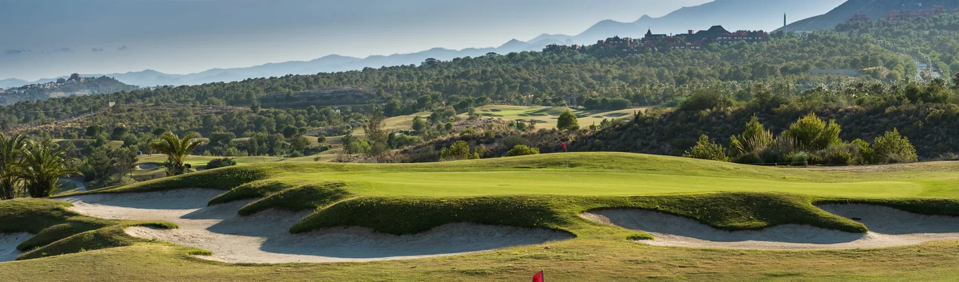 Poniente Course green and bunkers beneath wooded hills · On-site golf