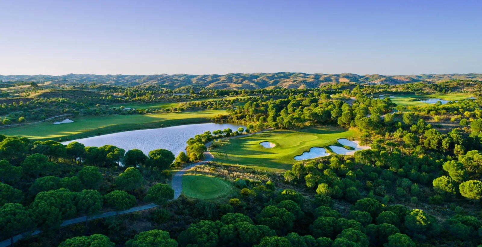 Panoramic view of Monte Rei North Course with a lake, greens and the surrounding Algarve countryside